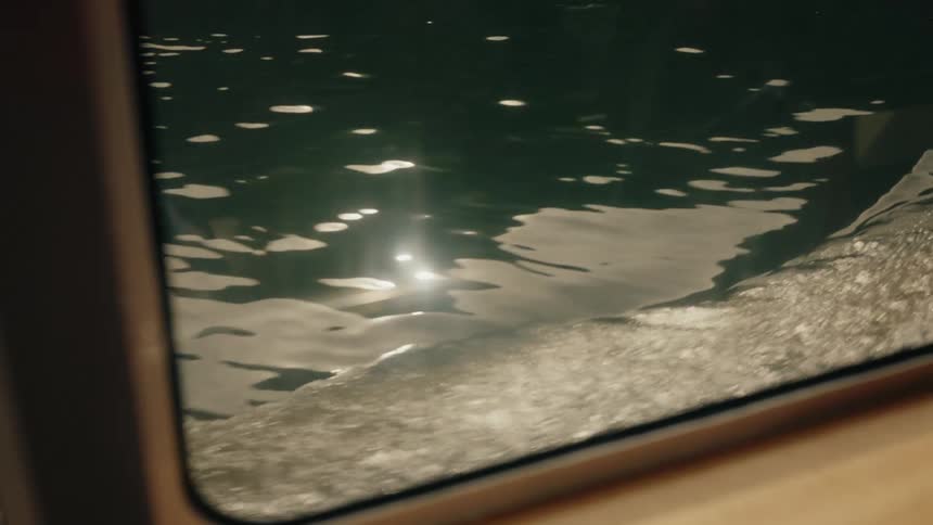 A view from a boat's cabin window shows shimmering light reflecting on the water as it moves
