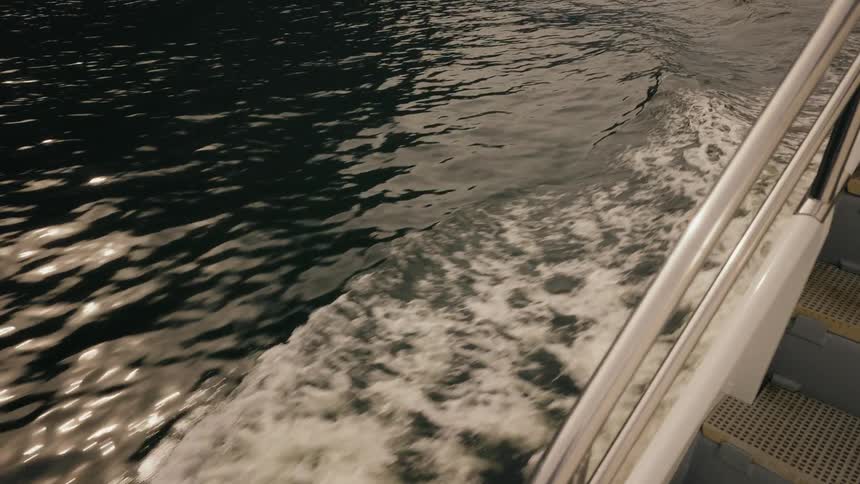 Close-up shot of the wake from a moving boat churning through dark, reflective waters