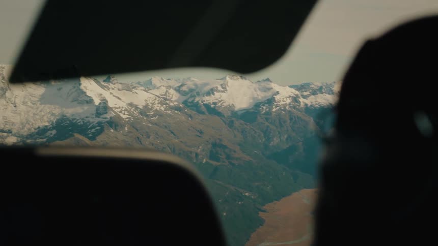 Slow rack focus from a pilot's silhouette to a magnificent snow-capped mountain range seen from an airplane cockpit