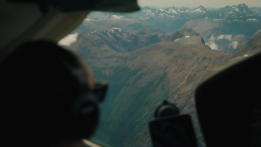 Over-the-shoulder view from a plane cockpit of a pilot flying over a rugged, snow-capped mountain range