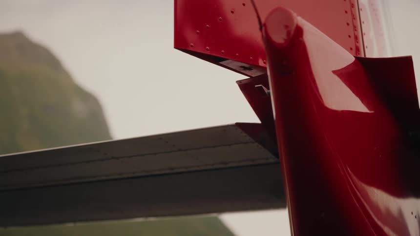 A close-up view of the tail fin and stabilizer of a red airplane with a misty mountain in the background
