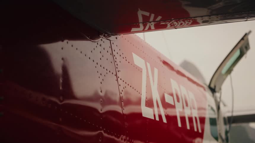 A slow-motion cinematic close-up of a red airplane's fuselage with an open door on an overcast day