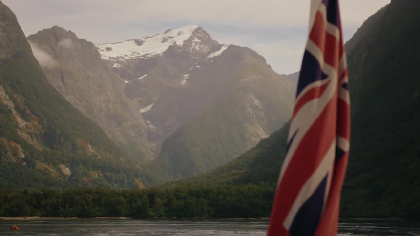 A Union Jack flag hangs in the foreground before the focus shifts to a majestic snow-capped mountain range in the distance