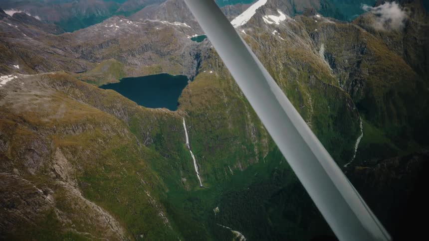 Breathtaking aerial view from a small plane flying over a majestic mountain range with a pristine lake and waterfalls below