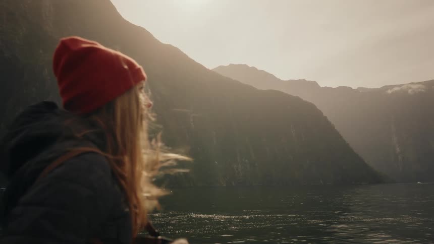 A female photographer in a red beanie captures the majestic misty fjord mountains on her camera