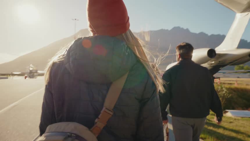A group of friends walk across a sunlit tarmac to board a private jet with mountains in the distance