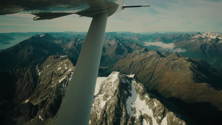 An epic aerial view from a small plane flying over a vast, snow-capped mountain range
