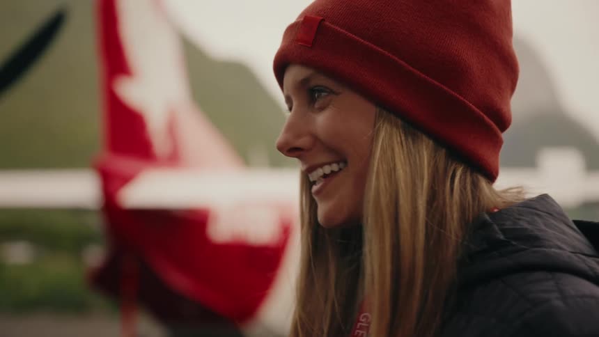 A happy woman in a red beanie smiles in slow motion in front of a small propeller plane