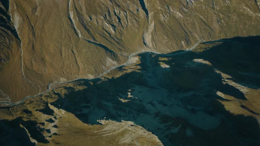 A stunning aerial time-lapse captures the dramatic movement of shadows across a rugged mountain valley and a winding river