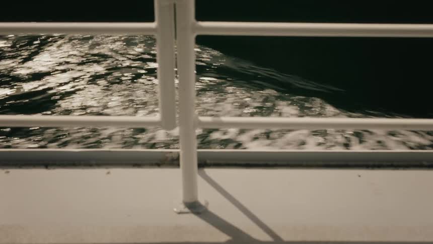 Sunlight shimmers on the dark water's surface as seen from the side of a moving boat