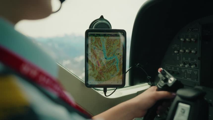 Over-the-shoulder view of a pilot using a digital tablet for GPS navigation while flying a small plane over a mountainous landscape