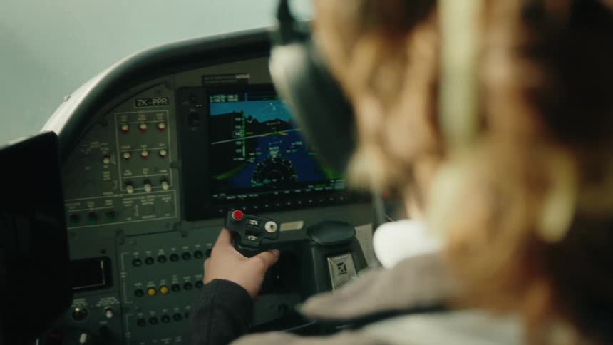 An over-the-shoulder view of a pilot holding the joystick while flying a small plane, with the navigation screen in focus