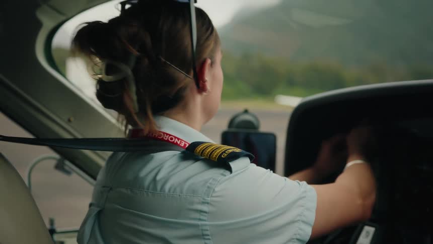 Focused female pilot in uniform sits in the cockpit of a small plane, performing her pre-flight checks