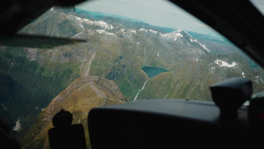 An awe-inspiring aerial view from a cockpit of a small plane flying over a vast, snow-capped mountain range with a pristine alpine lake