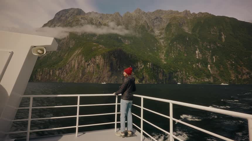 A tourist on a ferry cruise walks to the railing to admire and photograph the breathtaking mountain landscape of a fjord