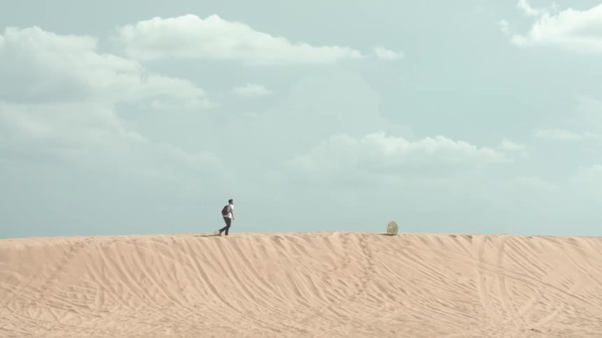 A man is hiking on a sand dune towards an object