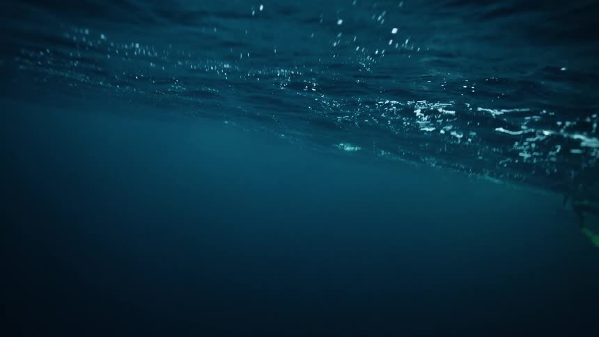 An underwater perspective of the deep blue ocean surface as a diver with fins swims by