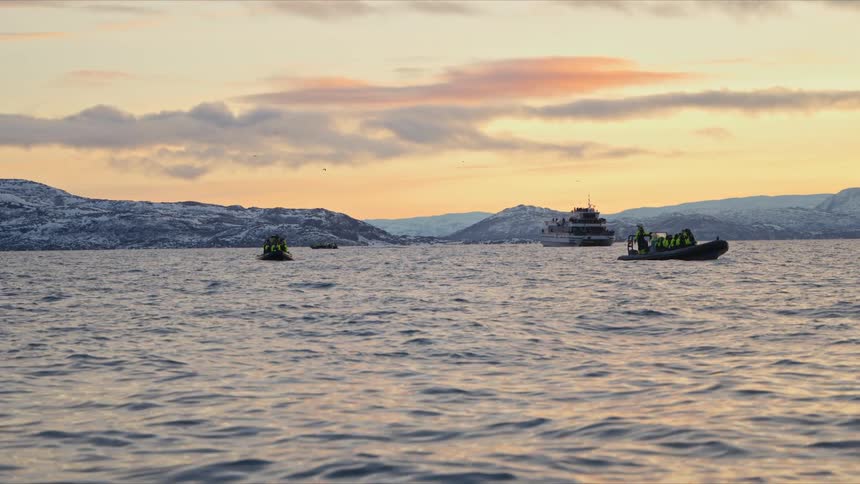 Adventurous tourists explore a scenic arctic fjord in inflatable boats during a beautiful sunset