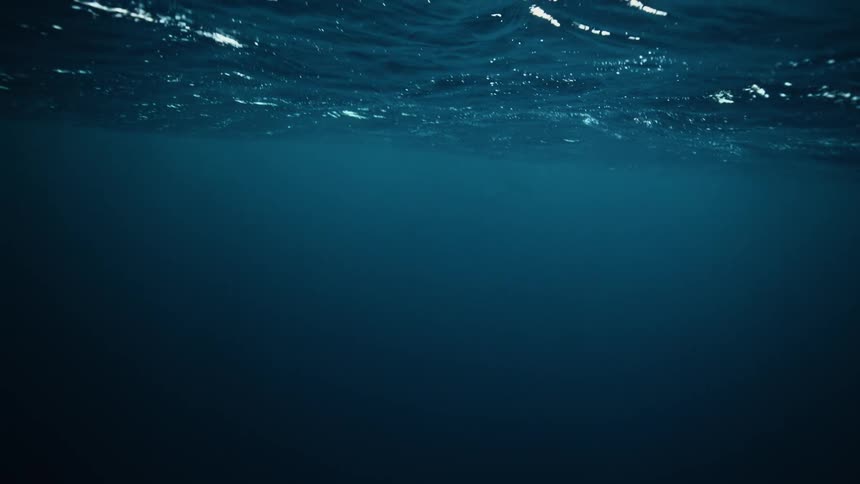 A mysterious and serene view from beneath the deep blue ocean surface as it ripples in slow motion
