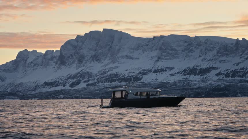 A modern motorboat drifts peacefully in a tranquil fjord, framed by the majestic snow-covered mountains of Norway under a warm sunset sky