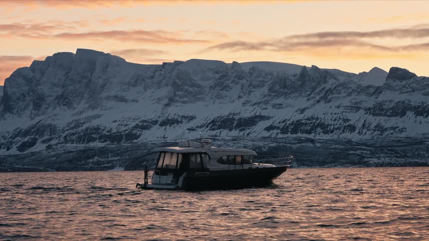 A lone yacht peacefully floats on the calm waters of a fjord at sunset, with a vast, snowy mountain range in the background