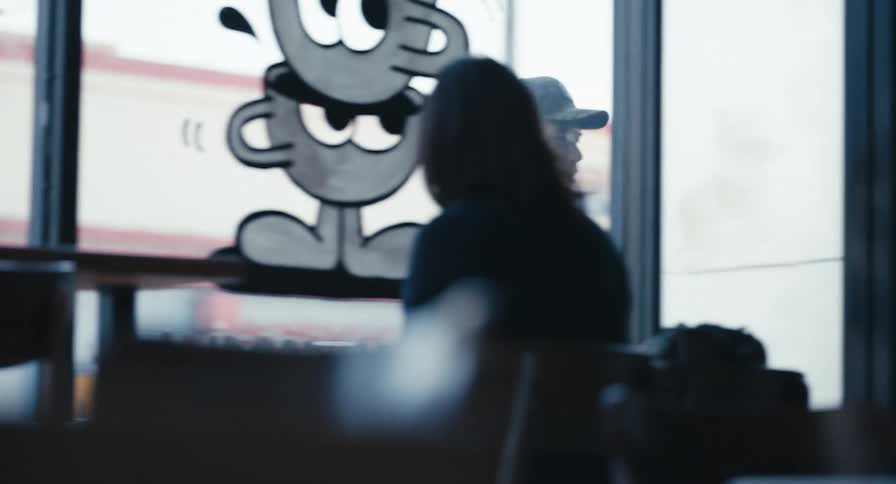 A man in a baseball cap talks on his phone as he walks past the window of a cafe and enters