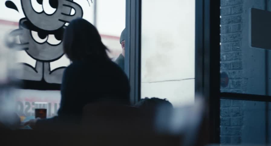 A man on a phone call walks past the window and enters a trendy urban coffee shop on a cloudy day