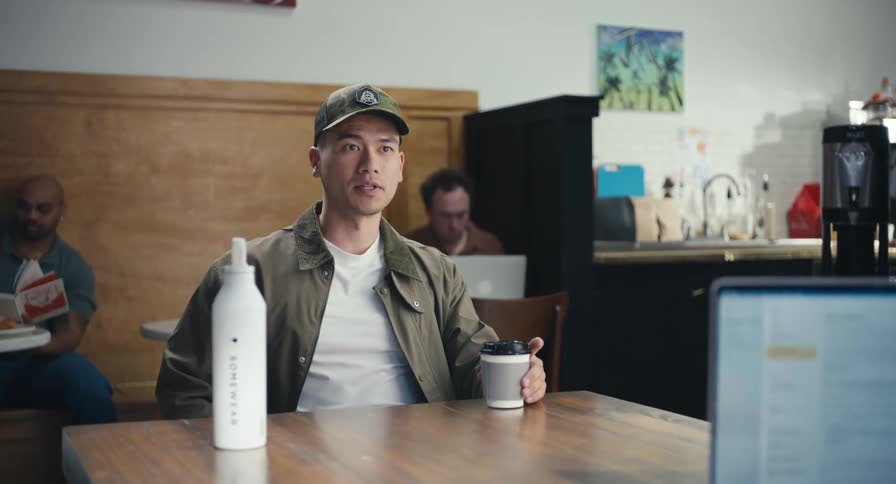 A young man in a baseball cap enjoys a coffee and engages in an enthusiastic conversation at a local coffee shop