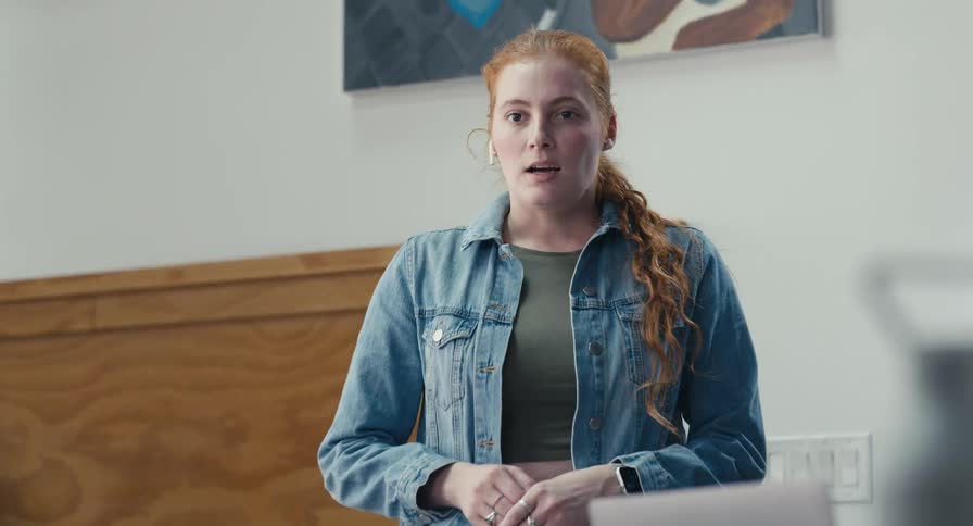 A young woman with red hair transitions from working to passionately addressing her colleagues during a meeting in a modern office