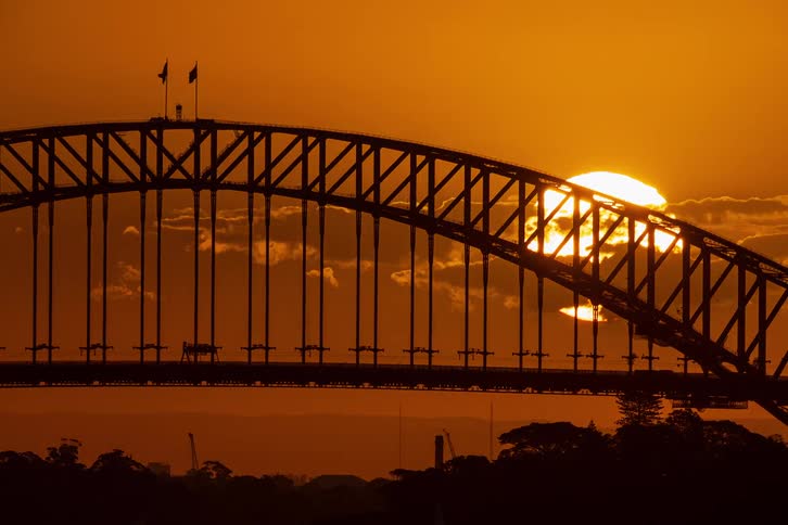 A stunning timelapse shows the sun setting behind the silhouetted Sydney Harbour Bridge against a fiery orange sky