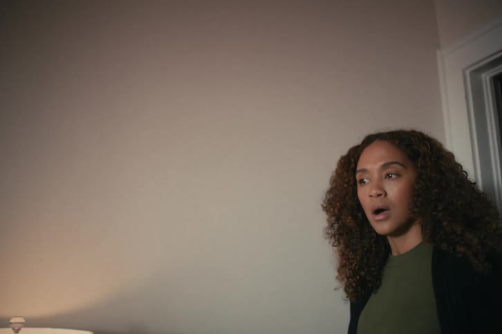 A woman stands in a dimly lit room with a look of shock and disbelief on her face