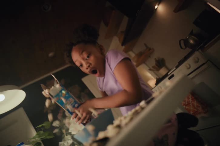 A young girl is shocked as she accidentally spills her marshmallow cereal all over the kitchen counter in slow motion
