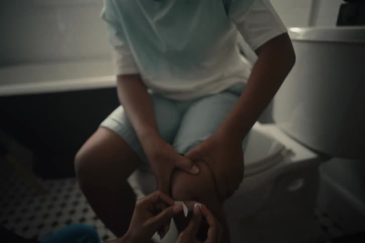 Close up of a parent applying a bandage to their young son's injured knee in the bathroom