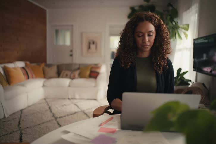 Focused mother working from home on a laptop as her children energetically play in a motion blur behind her