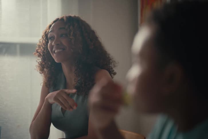 An African American mother smiles and talks to her young son as he enjoys a healthy snack at the dining table