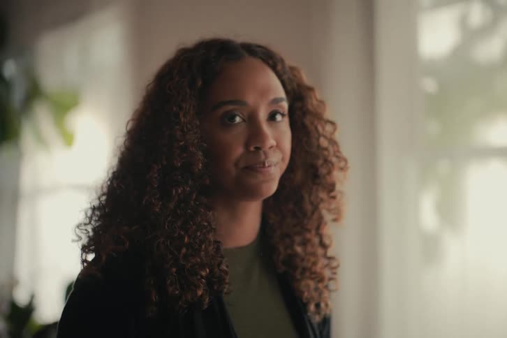 A confident woman with curly hair closes her laptop, ending her workday, and then looks thoughtfully into the camera before standing up