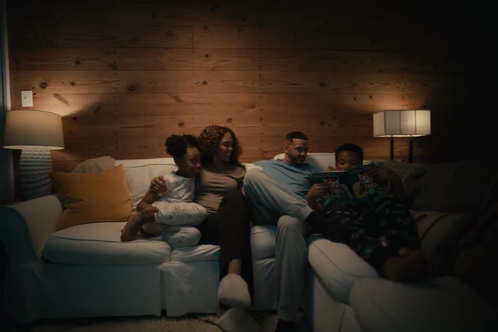 A loving family of four relaxes together on a couch at night in their cozy, dimly lit living room
