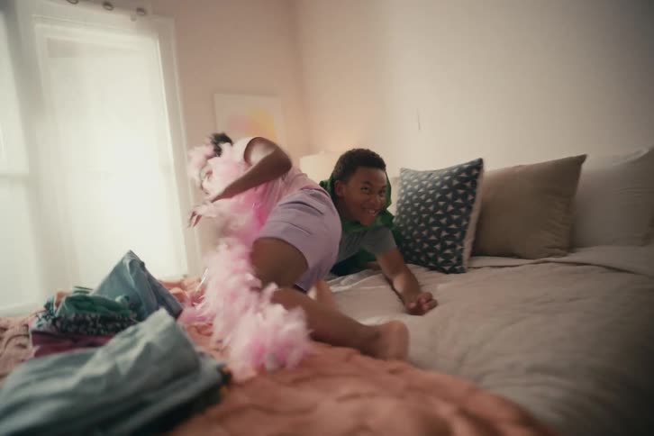 Slow motion shot of two young siblings in costume playing and jumping on a bed in their sunlit bedroom