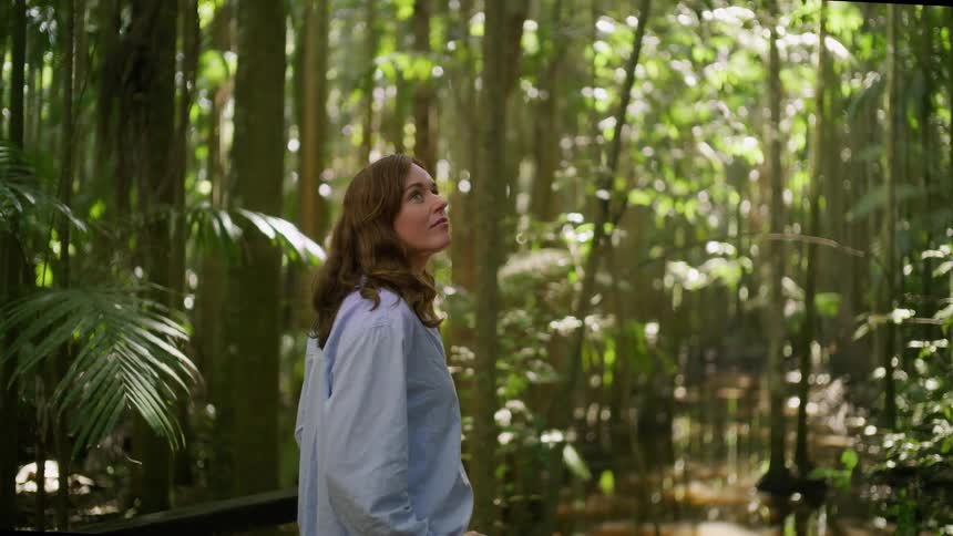 A serene woman takes in the beauty of a tropical rainforest, looking up with wonder at the verdant canopy