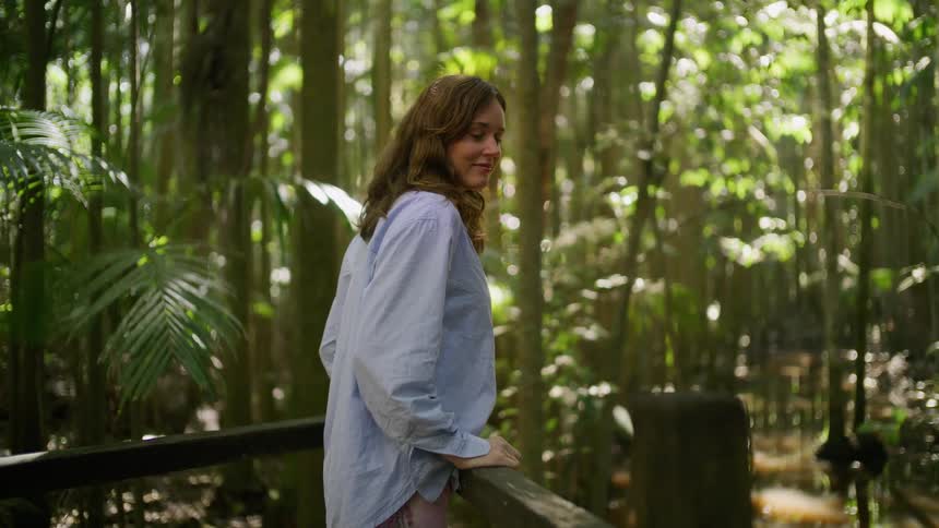 A serene woman takes a moment to appreciate the beauty of a sun-dappled tropical forest from a boardwalk