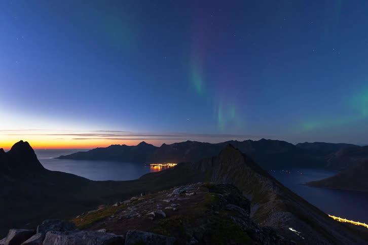 A stunning timelapse shows the Aurora Borealis dancing in the twilight sky over a majestic fjord and glowing coastal town
