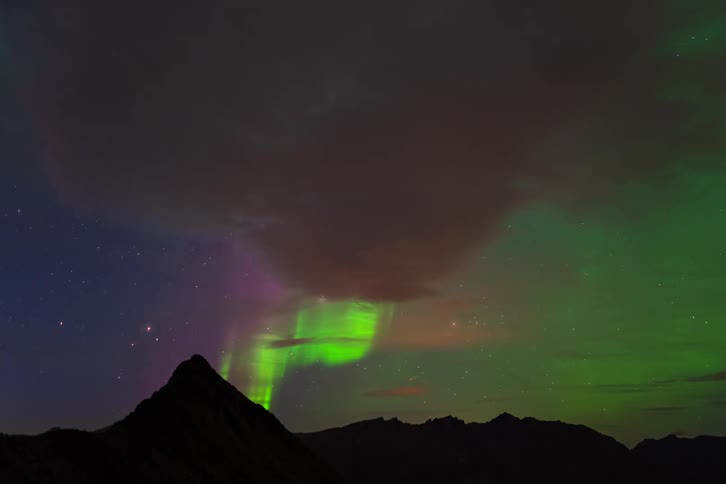 A time-lapse of the green and purple Northern Lights dancing in the starry night sky above silhouetted mountains