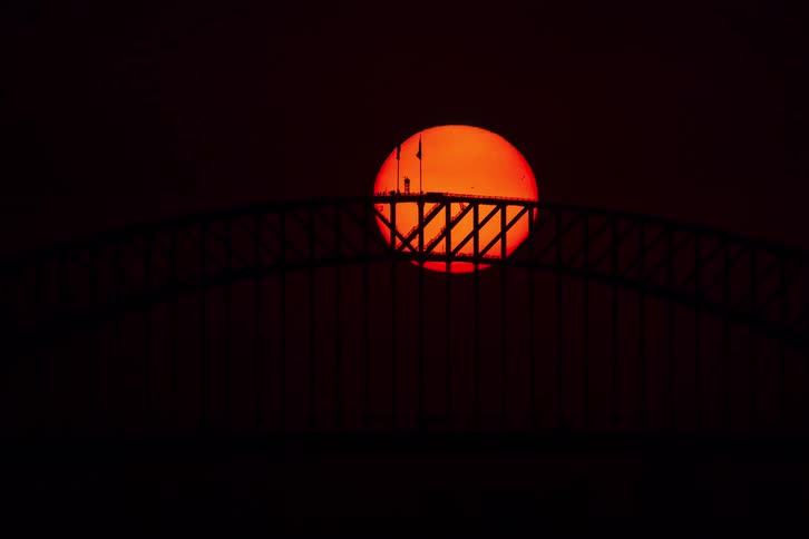 A dramatic time-lapse shows the blood-red sun setting behind the dark silhouette of the Sydney Harbour Bridge