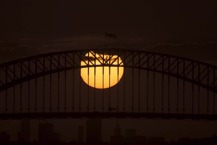 A dramatic time-lapse captures the sun setting behind the iconic Sydney Harbour Bridge silhouette as traffic crosses