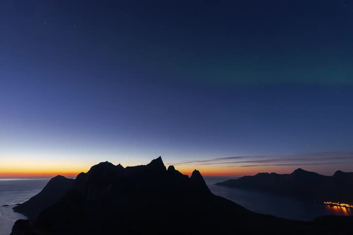 Stunning timelapse shows the green Aurora Borealis swirling and fading above coastal mountains as twilight gives way to a starry night