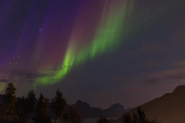 Time-lapse of the brilliant green and purple Aurora Borealis dancing across the starry night sky over a silhouetted mountain range
