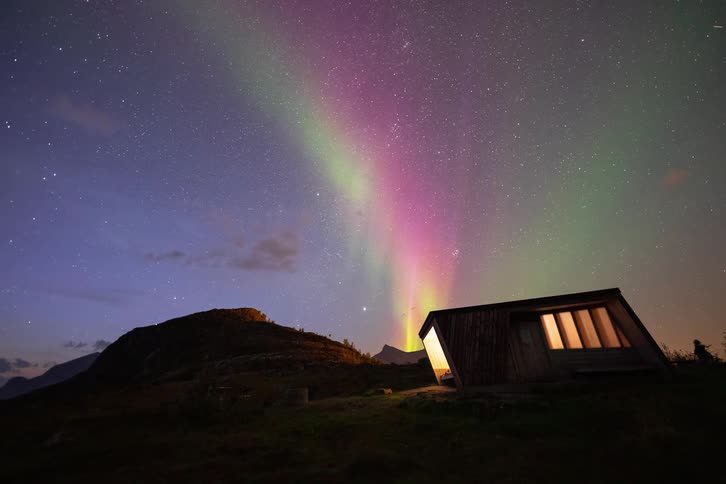 A stunning time-lapse of the colorful Aurora Borealis dancing in the starry night sky over a secluded modern cabin in the mountains