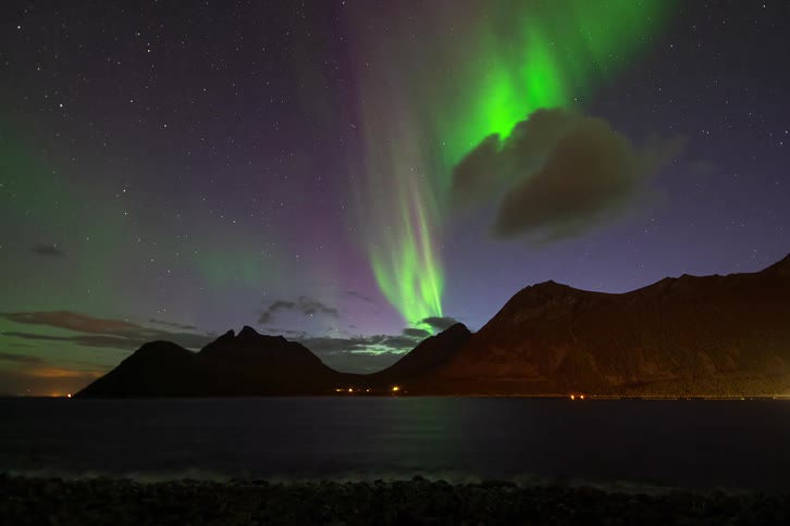 A stunning time-lapse captures the green and purple Aurora Borealis dancing in the starry night sky over mountains and a fjord