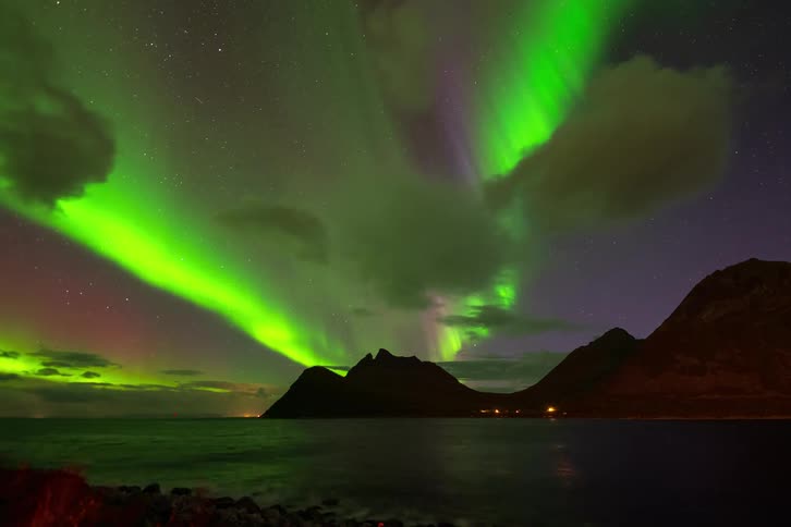 A stunning time-lapse of the vibrant green Aurora Borealis dancing above a mountain range and the ocean at night