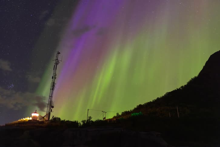 A stunning timelapse captures the vibrant green and purple Aurora Borealis dancing across the starry night sky above a communications tower on a hill